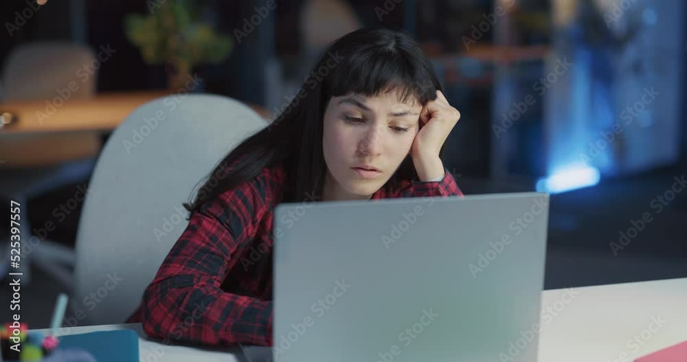 Overwhelmed young tired caucasian woman leaning on table looking on screen laptop with exhausted eyes overworking in corporate office. Nightlife.
