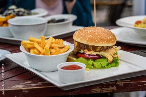 juicy pork burger with cheese, sauce and french fries on a table in a cafe. photo