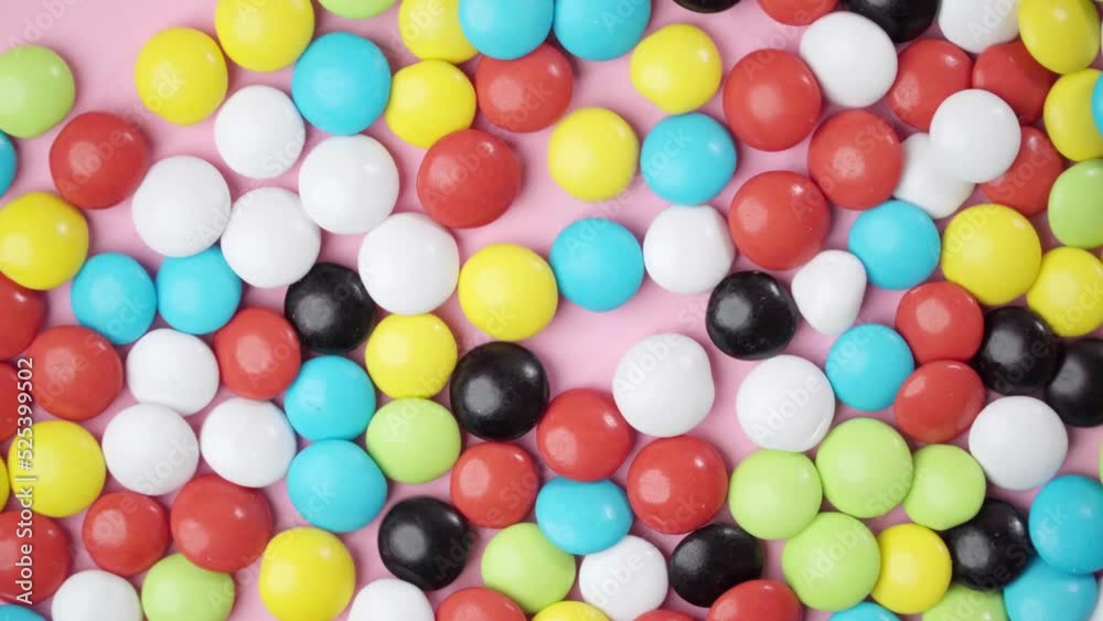 Multi-colored candy dragees move shaking against a pink background in motion Multi-colored candy dragees move shaking against a pink background in motion