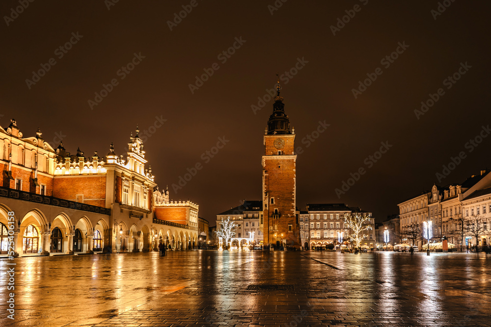 Krakow after rain,Poland.Main square with famous Christmas markets,Rynek Glowny at night with reflection,decorated timber huts,Xmas tree.Festive atmosphere,blurred people in motion,illuminated city