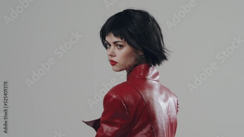 A woman dances in a stylish fashion red cloak with a beautiful make-up with black short hair in front of the camera