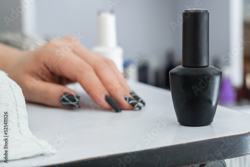close-up of matte black nail polish on a white manicure table  in the background a hand with black painted nails. concept of beauty and dark style. 