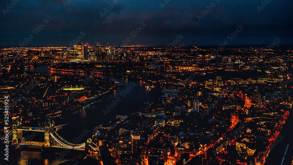 Aerial night view of west London with Tower Bridge over river Thames bottom left corner, illuminated buildings glowing in dark