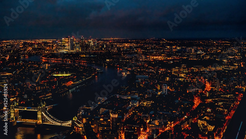 Aerial night view of west London with Tower Bridge over river Thames bottom left corner  illuminated buildings glowing in dark