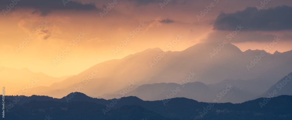 Amazing silhouettes of a mountains at colorful sunset in summer in Slovenia. Landscape with mountain ridges in fog, golden sunlight and clouds in the evening. Nature. Hills in sunlight. Scenery