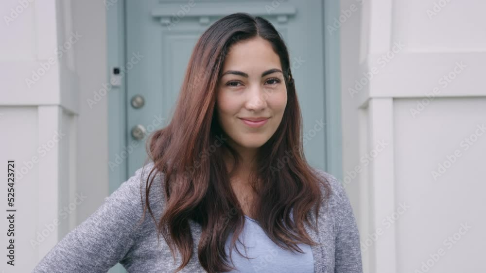 Beautiful woman smiles confidently at camera while standing by house front porch