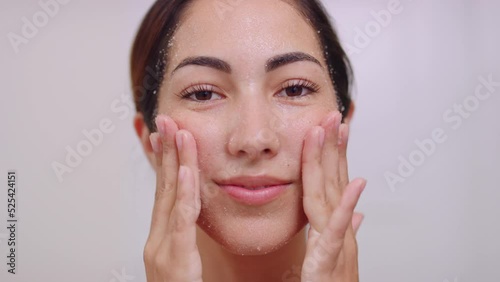 Pretty hispanic woman exfoliates face with white salt scrub in closeup