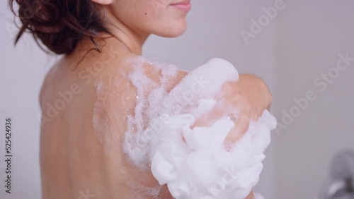 Close on woman's shoulder in shower as she slowly scrubs body wash bubbles