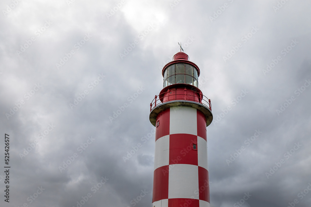 Exterior of a red and white steel and concrete lighthouse set against dramatic sky, nobody