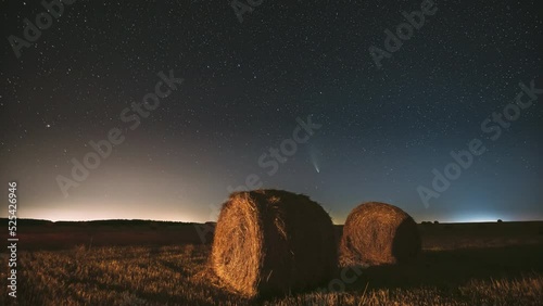 Comet Neowise C 2020 F3 In Night Starry Sky Above Haystacks In Summer Agricultural Field. Night Stars Above Rural Landscape With Hay Bales After Harvest. Agricultural Concept. 4K Timelapse. photo