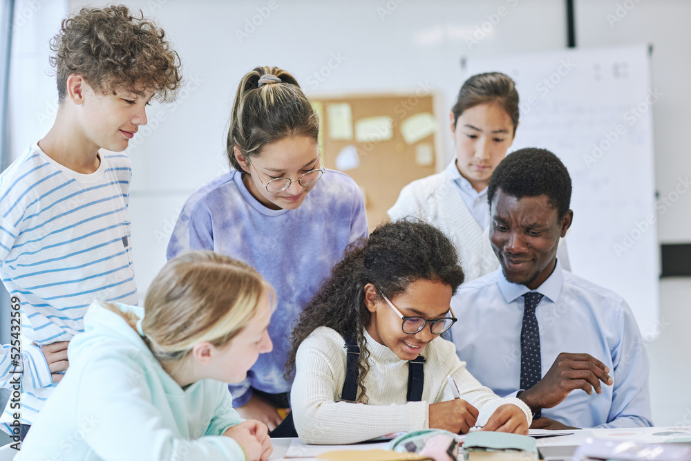 Diverse group of children smiling happily in school while working together with young male teacher Diverse group of children smiling happily in school while working together with young male teacher