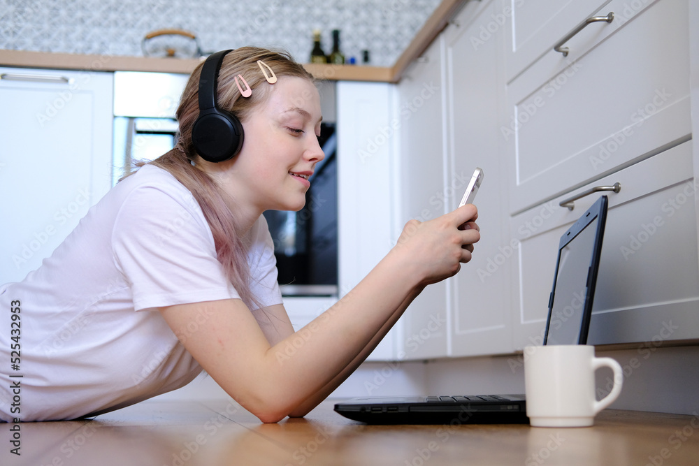 A young girl of 15-18 years old lies on the floor with a laptop and a telephone A young girl of 15-18 years old lies on the floor with a laptop and a telephone