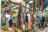 01.15.2021 Thessaloniki, Greece. Tourists or Greeks walking by a butcher's at Kapani Market. Raw meat hanging down. Sheep legs. High quality photo