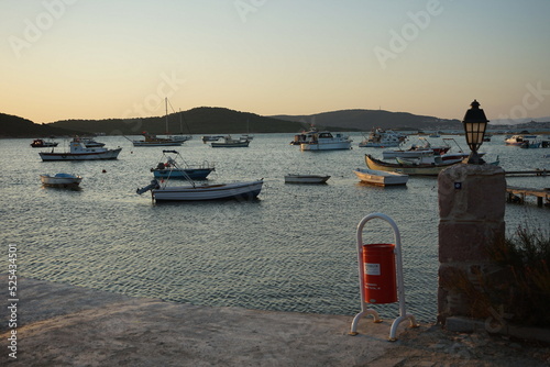 Roter städtischer Mülleimer und ankernde Boote und Yachten im Sommer im Licht der Abendsonne am Strand in der Bucht an der Küste von Ayvalik an Ägäischen Meer in der Provinz Balikesir in der Türkei photo