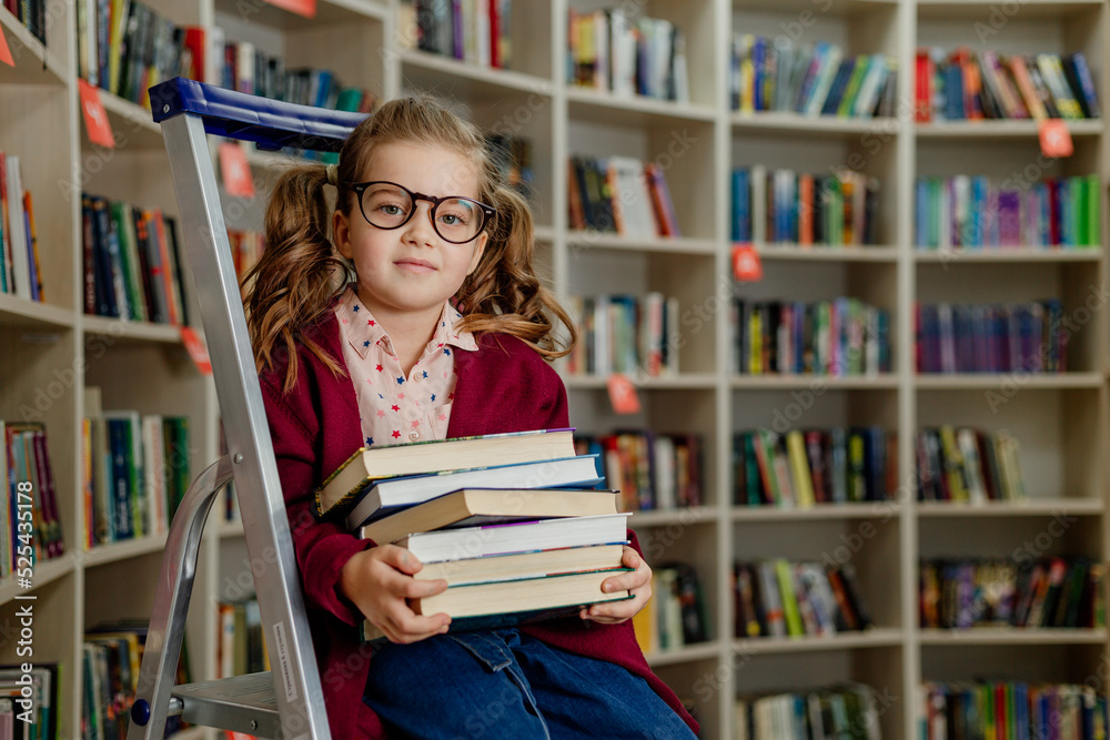 girl with glasses reads a book sitting on a stepladder in the library girl with glasses reads a book sitting on a stepladder in the library