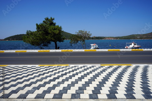 Küstenstraße mit Bäumen und Fahrbahnmarkierung im Sommer vor blauem Himmel und Sonnenschein in Ayvalik am Ägäischen Meer in der Provinz Balikesir in der Türkei photo