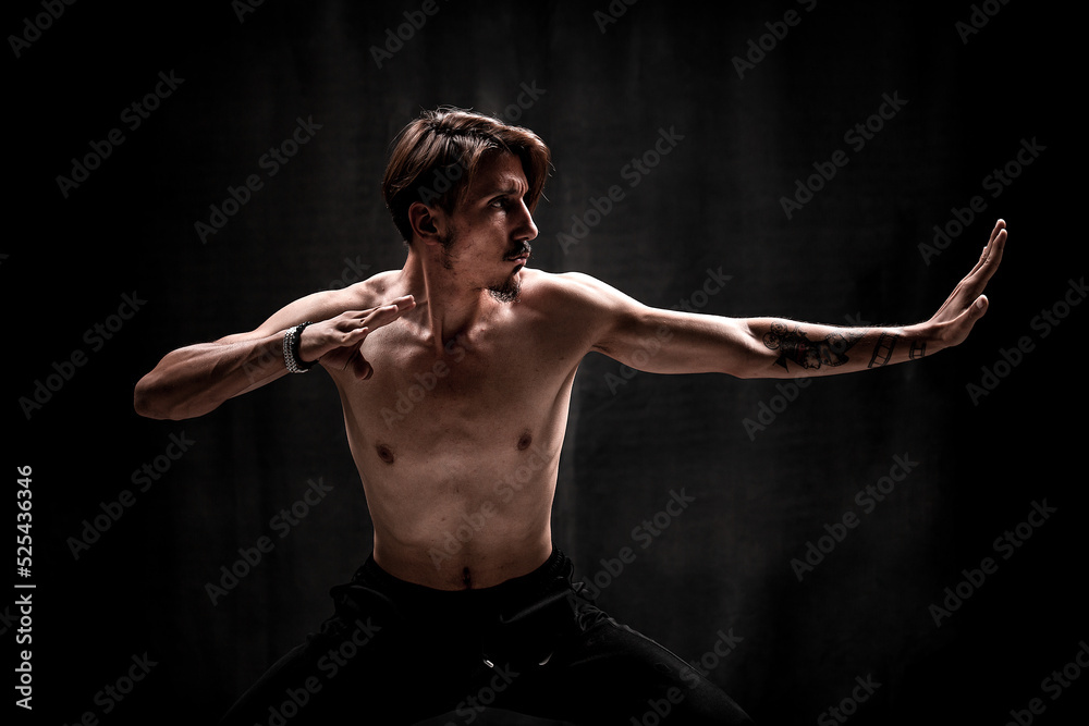 Fototapeta premium Asian man fighter practices martial arts on black background. Kung fu and karate pose. In addition, discipline, concentration, meditation, etc. concepts