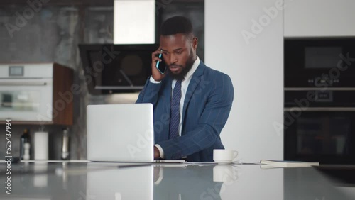 Wallpaper Mural African-American businessman talk on cellphone and work with laptop and documents in modern kitchen  Torontodigital.ca