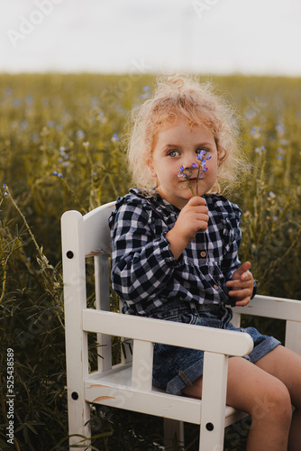 Dziecko o blond włosach siedzi na krześle i wącha kwiatki które trzyma w rękach