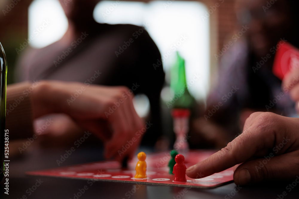 Obraz premium Close up of people hands moving plastic figurines on game table while sitting at table. Group of friends playing boardgames together while enjoying snacks and cold beverages.
