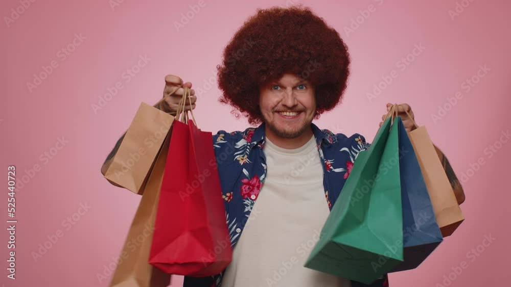 Happy tourist man with lush hair showing shopping bags, advertising discounts, smiling looking amazed with low prices, shopping on Black Friday holidays. Young bearded guy boy on blue background Happy tourist man with lush hair showing shopping bags, advertising discounts, smiling looking amazed with low prices, shopping on Black Friday holidays. Young bearded guy boy on blue background