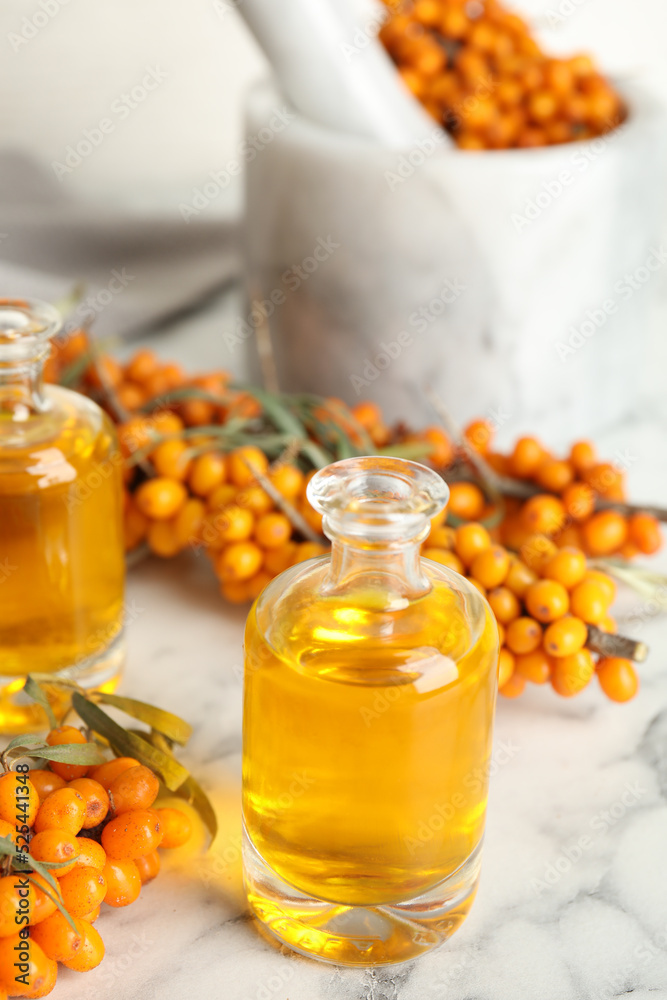 Natural sea buckthorn oil and fresh berries on white marble table Natural sea buckthorn oil and fresh berries on white marble table