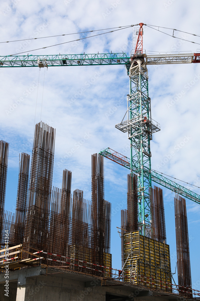 Naklejka premium Tower crane near building under construction against cloudy sky