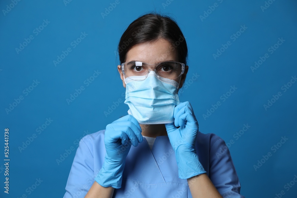 Doctor in protective mask, medical gloves and glasses against blue background Doctor in protective mask, medical gloves and glasses against blue background