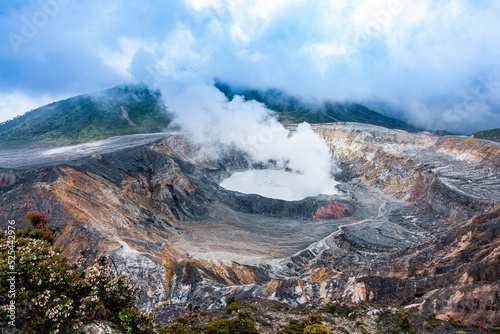 horizontal photo of the Poas volcano from a distance in Costa Rica, a wide shot of a volcano spewing steam surrounded by stones.
