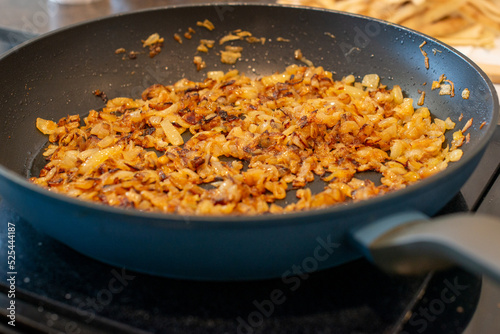 Photos A large black colored iron frying pan full of sweet white onions minced and chopped into being fried or sauteed in butter