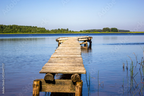 Wooden pier in summer in the forest on the lake.Old wooden pier made of boards in reeds.Rustic,natural landscape. photo