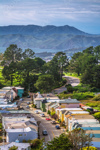 The view on the street in San Francisco with parked cars and hills with ocean in the background