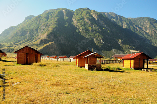 Several small wooden houses in a picturesque valley surrounded by mountains on an early autumn morning.