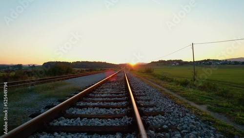 LOW ANGLE: Moving above glowing golden lit railroad tracks in autumn morning. Countryside railway passing gorgeous hilly landscape. Overview of railway tracks and junction near train station.