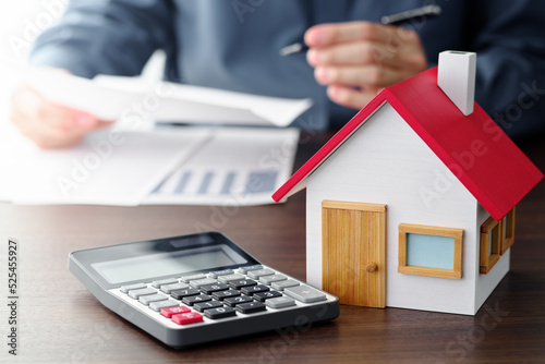 Person looking through estate contract. House model and calculator on table.