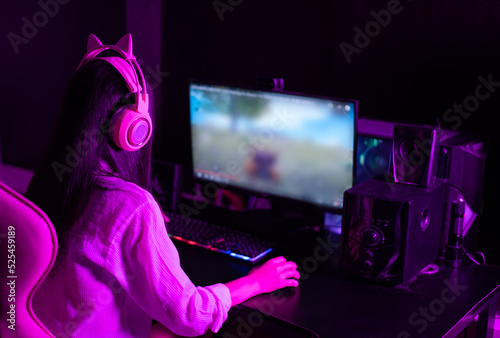Photography Asian woman wearing headphones playing a first-person shooter online video game on her computer