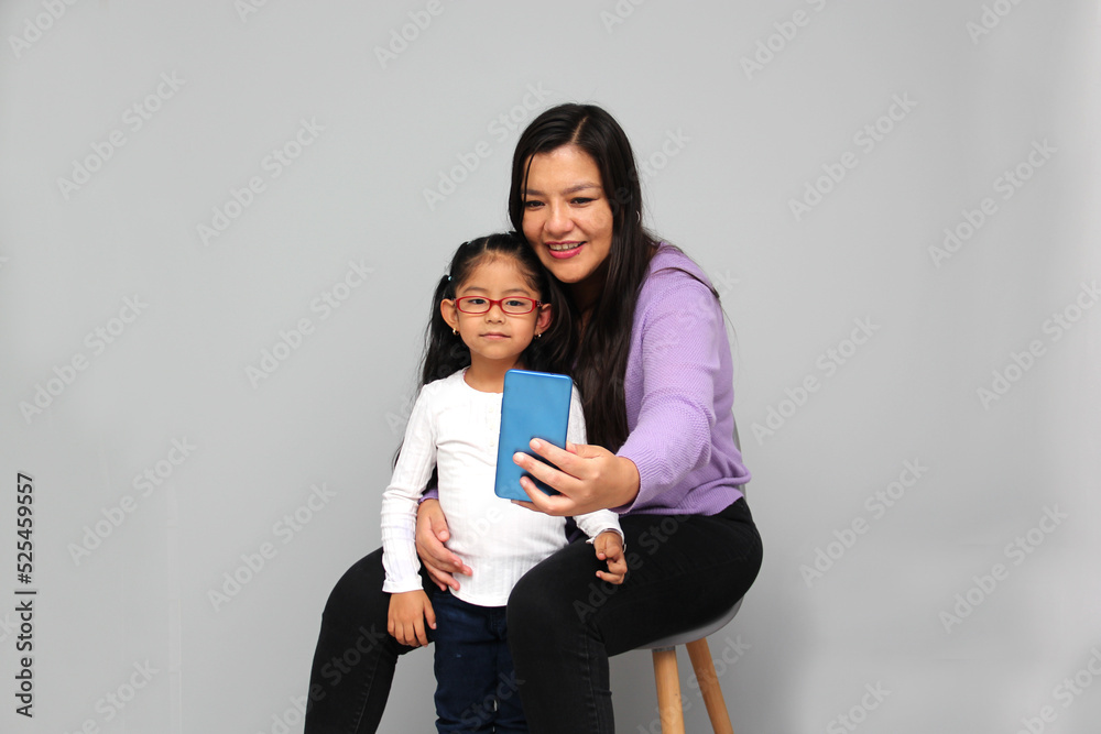 Single divorced Latina mom and daughter use cell phone to video call, take selfies, play video games, and shop online Single divorced Latina mom and daughter use cell phone to video call, take selfies, play video games, and shop online