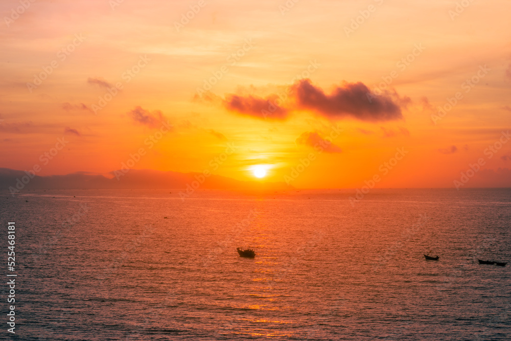 Beautiful cloudscape over the sea, sunrise shot. Lonely boats. Vung Tau beach, Vietnam with beautiful yellow sunrise sky, sun and clouds in orange and blue tones.