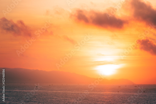 Beautiful cloudscape over the sea, sunrise shot. Lonely boats. Vung Tau beach, Vietnam with beautiful yellow sunrise sky, sun and clouds in orange and blue tones. © CravenA