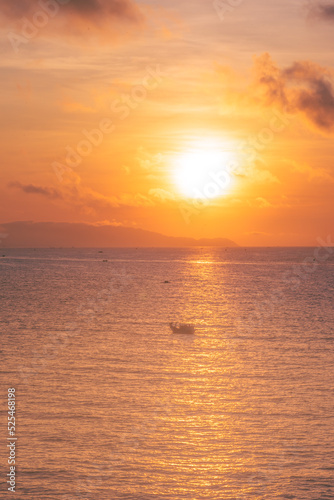 Beautiful cloudscape over the sea, sunrise shot. Lonely boats. Vung Tau beach, Vietnam with beautiful yellow sunrise sky, sun and clouds in orange and blue tones.