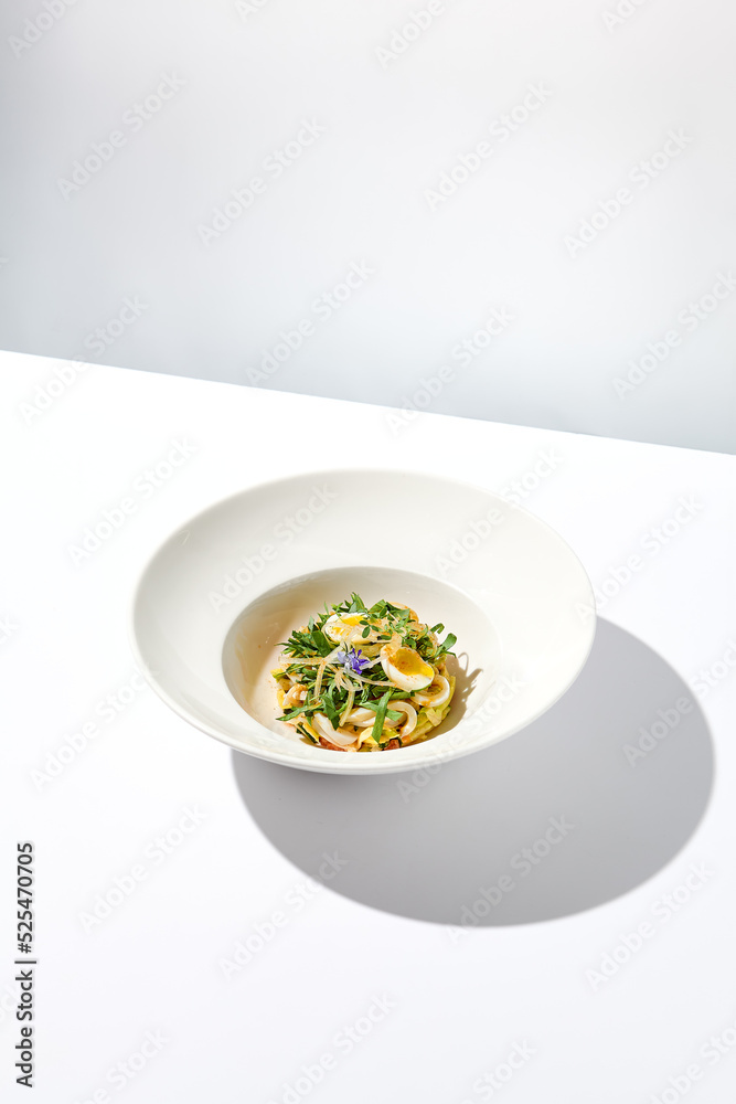 Healthy salad with squid and avocado on white plate with harsh shadows. Calamari salad with vegetables and eggs on white background with shadows of leaves. Summer food menu. Healthy salad with squid and avocado on white plate with harsh shadows. Calamari salad with vegetables and eggs on white background with shadows of leaves. Summer food menu.