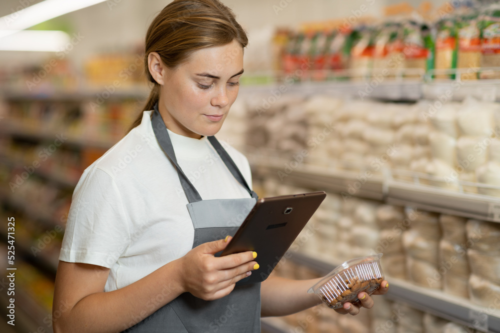 Portrait of a sales clerk wearing apron using a digital tablet with store shelves on background.