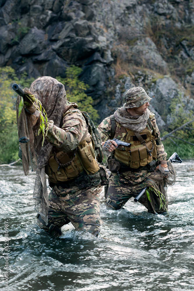 Fototapeta premium Vertical photo of a two mercenary soldiers ford a river during a sabotage operation.