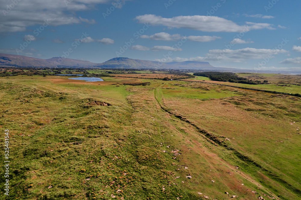 Naklejka premium Green field and Benbulben flat top mountain in county Sligo, Ireland, Irish landscape and nature scenery. Blue cloudy sky. Aerial image.