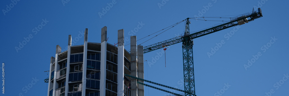 Fototapeta premium Construction crane standing near modern building against blue sky