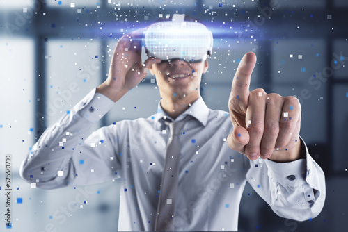 Attractive young european man pointing at abstract hologram with VR glasses in blurry office interior. Augmented reality and cyberspace concept.