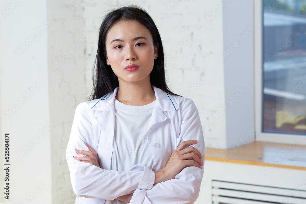Asian positive doctor woman in white medical gown with stethoscope against clinic interior indoor background portrait Asian positive doctor woman in white medical gown with stethoscope against clinic interior indoor background portrait