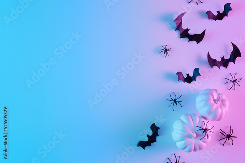 Creative flat lay Halloween background with bats silhouettes and pumpkins painted in vibrant gradient holographic neon colors. Copy space. Minimal season holiday concept.