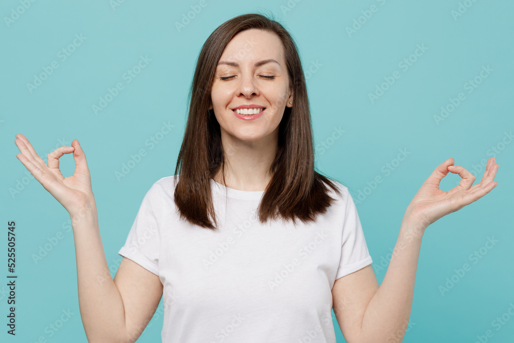 Young spiritual tranquil woman 20s she wear white t-shirt hold spread hands in yoga om aum gesture relax meditate try to calm down isolated on plain pastel light blue cyan background studio portrait. Young spiritual tranquil woman 20s she wear white t-shirt hold spread hands in yoga om aum gesture relax meditate try to calm down isolated on plain pastel light blue cyan background studio portrait.