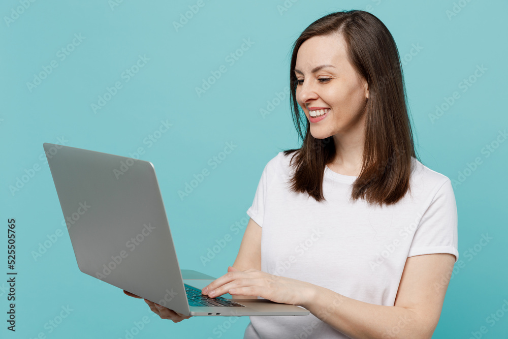 Young smiling happy fun caucasian woman 20s she wearing white t-shirt hold use work on laptop pc computer isolated on plain pastel light blue cyan background studio portrait. People lifestyle concept. Young smiling happy fun caucasian woman 20s she wearing white t-shirt hold use work on laptop pc computer isolated on plain pastel light blue cyan background studio portrait. People lifestyle concept.